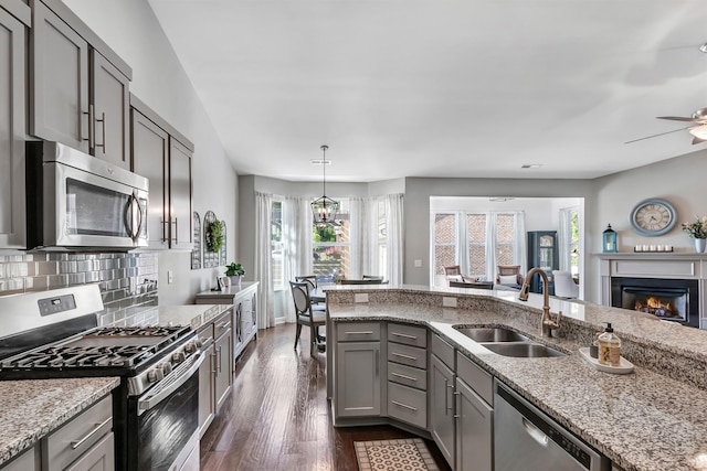 kitchen with appliances with stainless steel finishes, a sink, gray cabinetry, a lit fireplace, and dark wood-type flooring