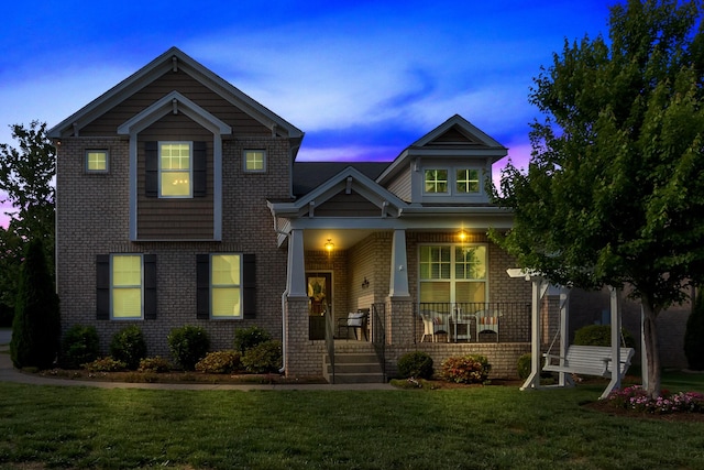 view of front of house with covered porch, a front yard, and brick siding