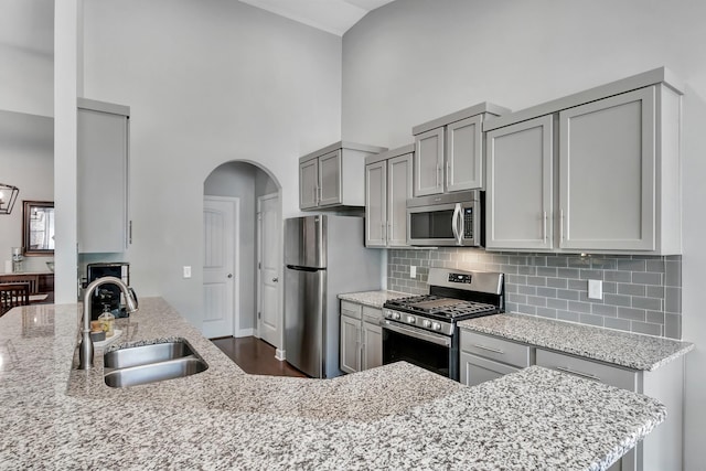 kitchen featuring stainless steel appliances, a sink, high vaulted ceiling, gray cabinets, and light stone countertops