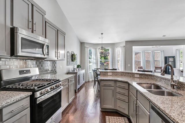 kitchen featuring stainless steel appliances, a sink, gray cabinets, and light stone counters