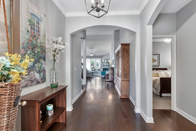 hall featuring dark wood finished floors, arched walkways, baseboards, and ornamental molding