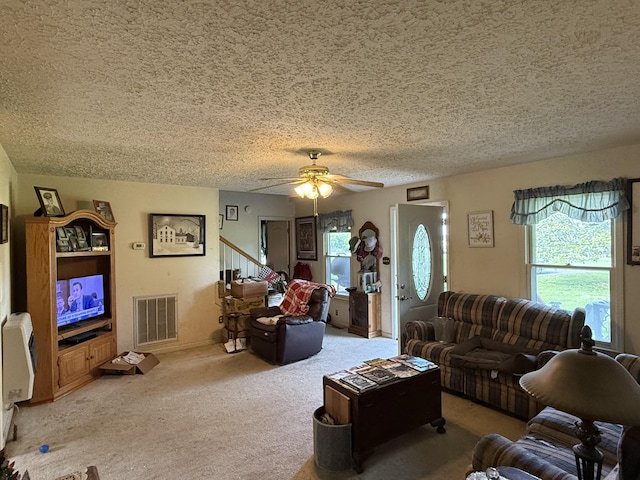 living room with a textured ceiling, carpet, a ceiling fan, and stairs