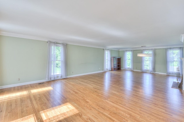 empty room featuring crown molding, light wood-style flooring, plenty of natural light, and baseboards