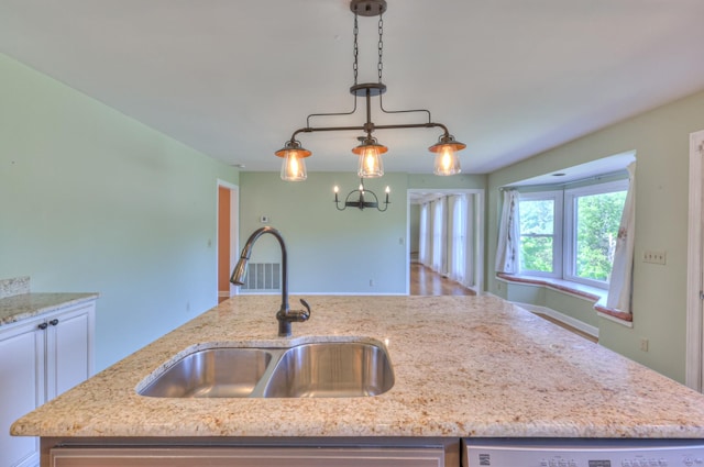 kitchen with a sink, light stone countertops, dishwashing machine, and a chandelier