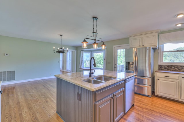 kitchen featuring a sink, appliances with stainless steel finishes, light stone counters, and light wood finished floors