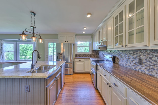 kitchen featuring appliances with stainless steel finishes, a sink, under cabinet range hood, dark stone countertops, and light wood-type flooring