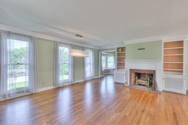 unfurnished living room featuring built in shelves, light wood-style flooring, a brick fireplace, ornamental molding, and baseboards