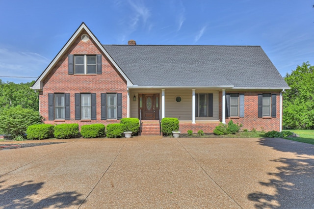 view of front of house with a chimney, brick siding, a porch, and roof with shingles
