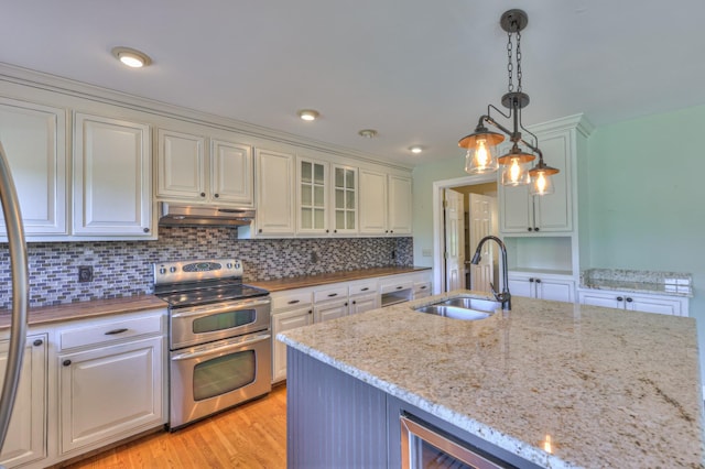 kitchen with a sink, double oven range, under cabinet range hood, tasteful backsplash, and white cabinets