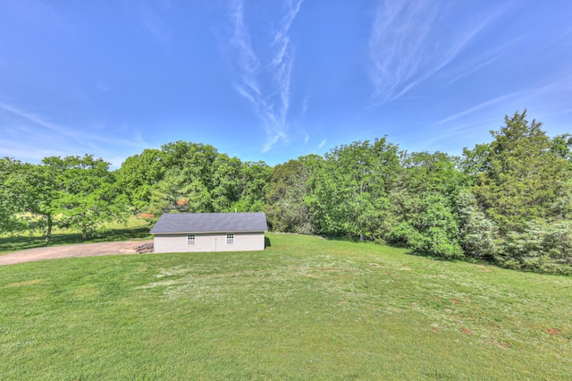 view of grassy yard with driveway and a view of trees
