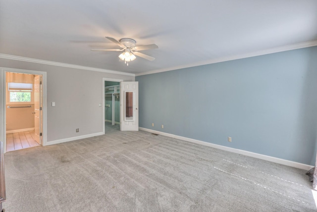 unfurnished bedroom featuring crown molding, light carpet, baseboards, a walk in closet, and connected bathroom