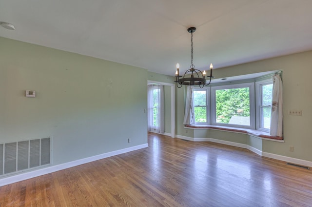 empty room with a chandelier, wood finished floors, and baseboards