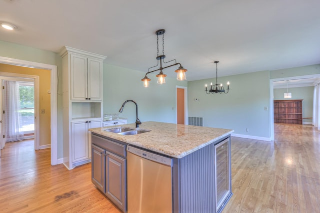 kitchen with stainless steel dishwasher, a sink, light wood-type flooring, light stone counters, and hanging light fixtures