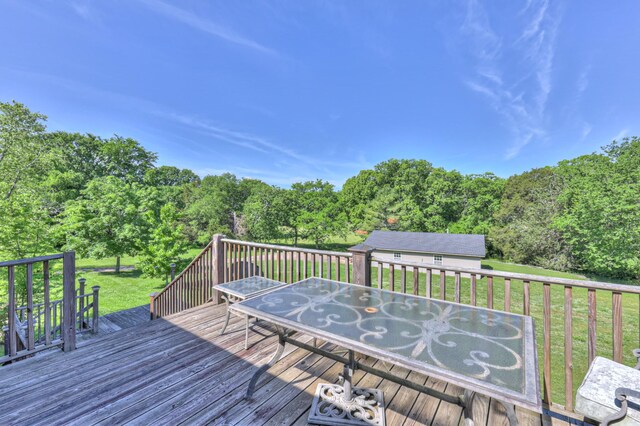 wooden deck with outdoor dining area, a lawn, and a forest view