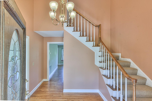 entrance foyer featuring a chandelier, a high ceiling, stairs, wood finished floors, and baseboards