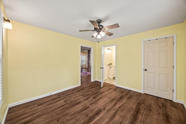 unfurnished bedroom featuring dark wood-type flooring, baseboards, ensuite bathroom, and a ceiling fan