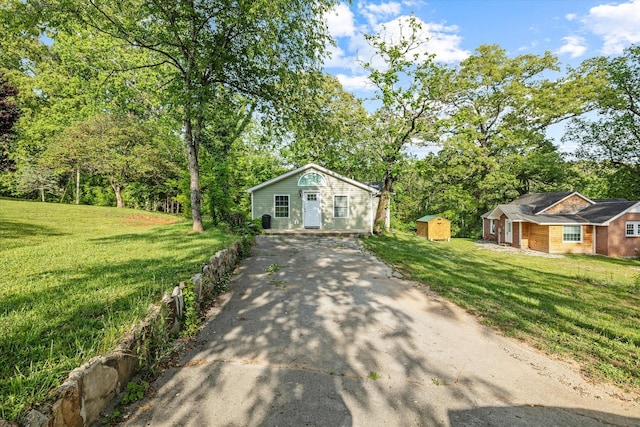 view of front of property featuring asphalt driveway, a shed, an outbuilding, and a front yard