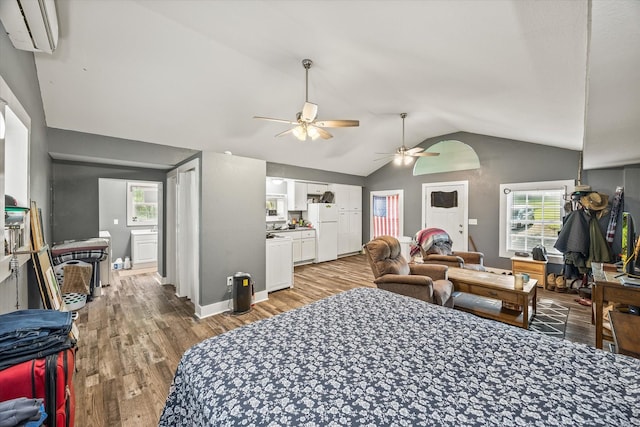 bedroom with freestanding refrigerator, vaulted ceiling, light wood-style flooring, an AC wall unit, and multiple windows