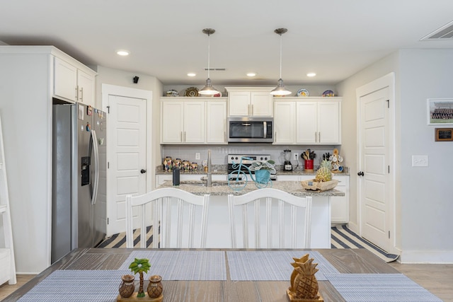 kitchen with appliances with stainless steel finishes, tasteful backsplash, an island with sink, white cabinets, and recessed lighting
