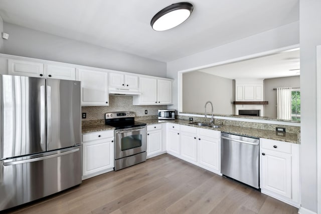 kitchen featuring appliances with stainless steel finishes, a sink, under cabinet range hood, white cabinetry, and stone counters