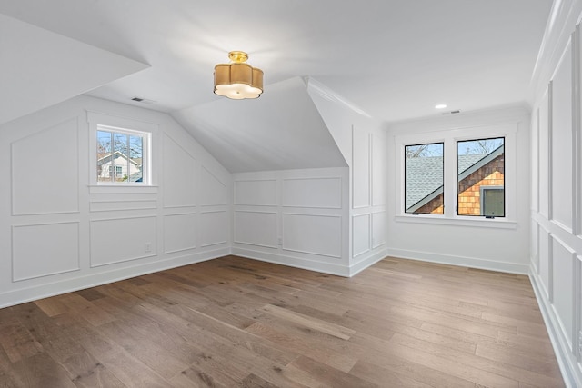 bonus room with a decorative wall, light wood-style floors, and vaulted ceiling