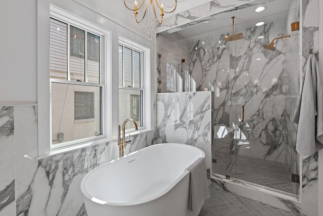 bathroom with tile walls, a chandelier, a marble finish shower, and a freestanding tub