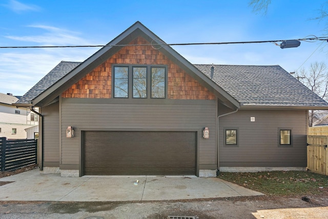view of front facade with fence, an attached garage, roof with shingles, and concrete driveway