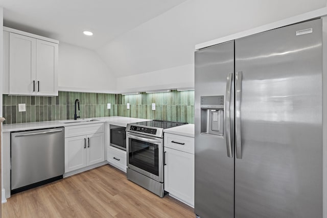 kitchen featuring stainless steel appliances, a sink, lofted ceiling, decorative backsplash, and white cabinets