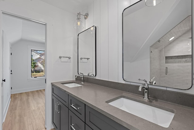 bathroom featuring lofted ceiling, wood finished floors, double vanity, a shower stall, and baseboards