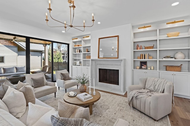 living room featuring recessed lighting, built in shelves, wood finished floors, a fireplace with flush hearth, and a chandelier