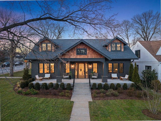 craftsman inspired home featuring a yard, covered porch, roof with shingles, and brick siding