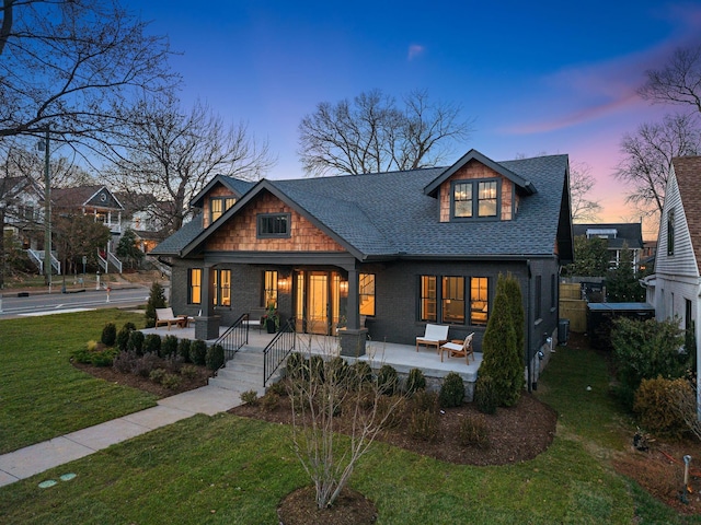view of front of house with a shingled roof, a yard, and a porch