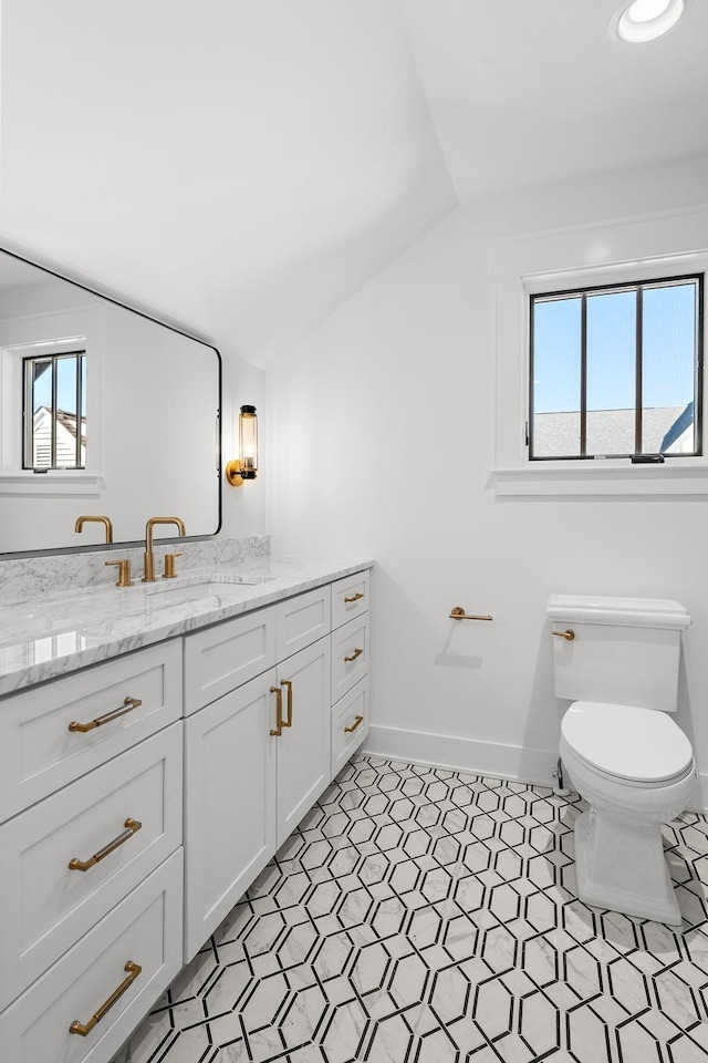 bathroom featuring lofted ceiling, toilet, plenty of natural light, baseboards, and vanity