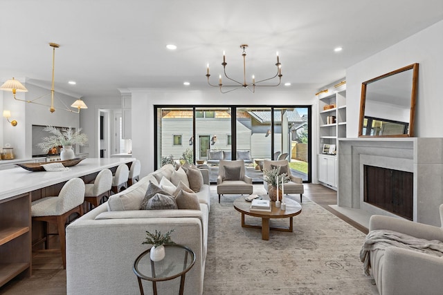 living room with recessed lighting, a chandelier, a premium fireplace, built in shelves, and crown molding