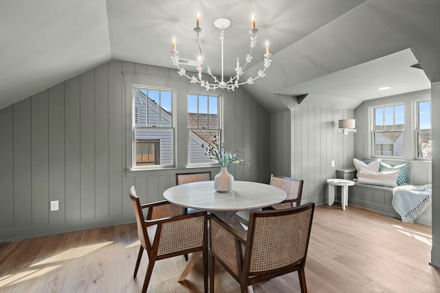 dining space featuring vaulted ceiling, light wood-type flooring, a chandelier, healthy amount of natural light, and wood walls