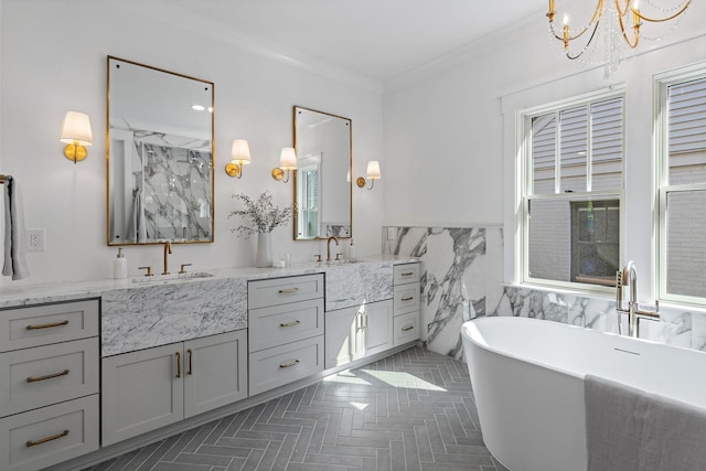 bathroom with a chandelier, ornamental molding, a freestanding bath, double vanity, and a wainscoted wall