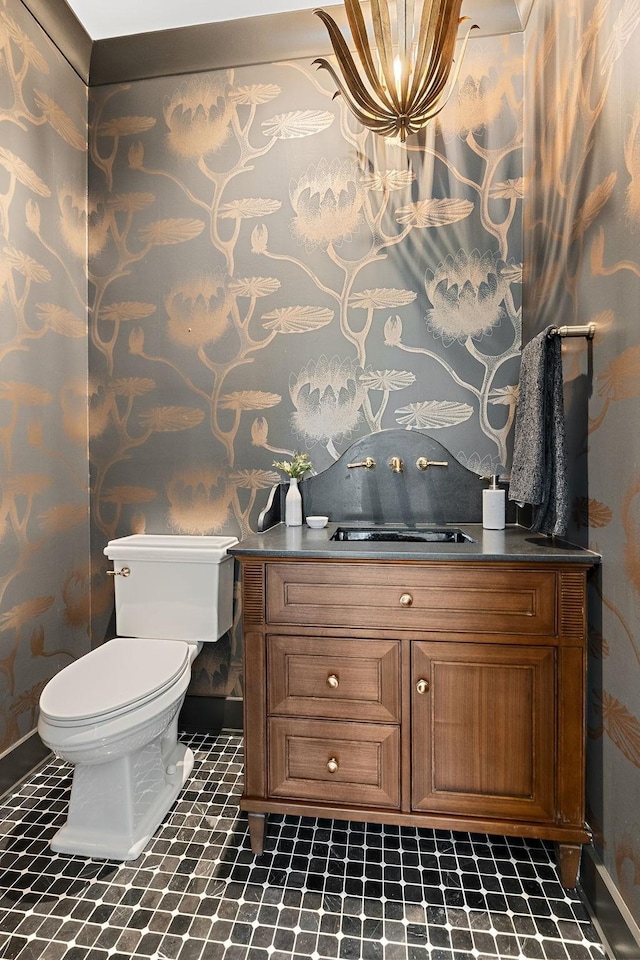 bathroom with wallpapered walls, toilet, vanity, and baseboards