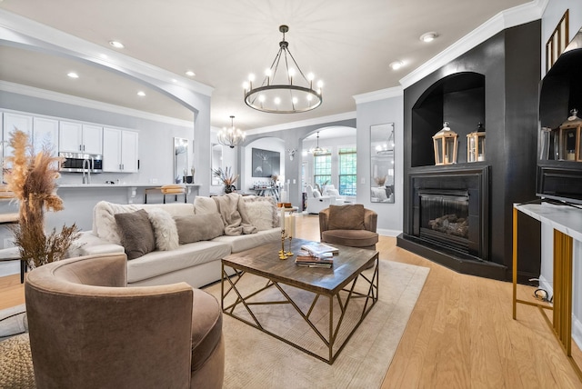 1113 Chickadee Cir, Hermitage, TN 37076 - living room featuring a chandelier, arched walkways, light wood-style floors, crown molding, and a glass covered fireplace