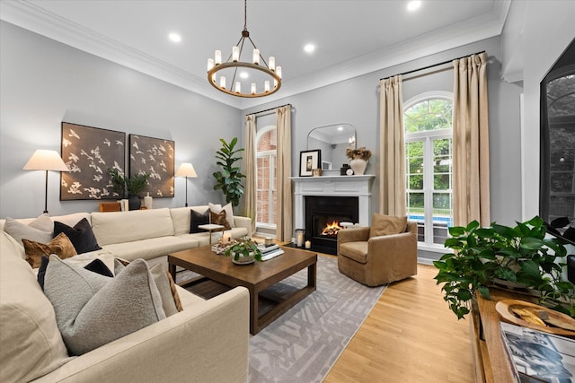 living area with wood finished floors, a lit fireplace, a chandelier, ornamental molding, and recessed lighting