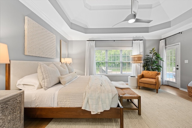 bedroom with a raised ceiling, crown molding, access to exterior, wood finished floors, and ceiling fan