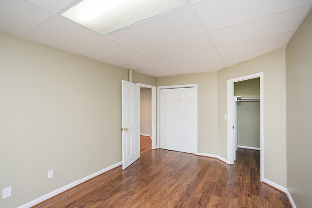 unfurnished bedroom with a paneled ceiling, a closet, wood finished floors, and baseboards
