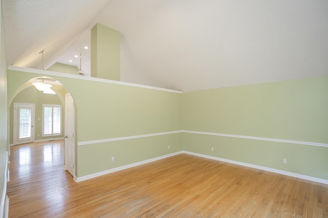 empty room featuring vaulted ceiling, light wood-style flooring, baseboards, and arched walkways