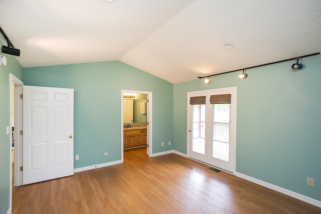 unfurnished bedroom featuring access to outside, wood finished floors, lofted ceiling, a textured ceiling, and rail lighting