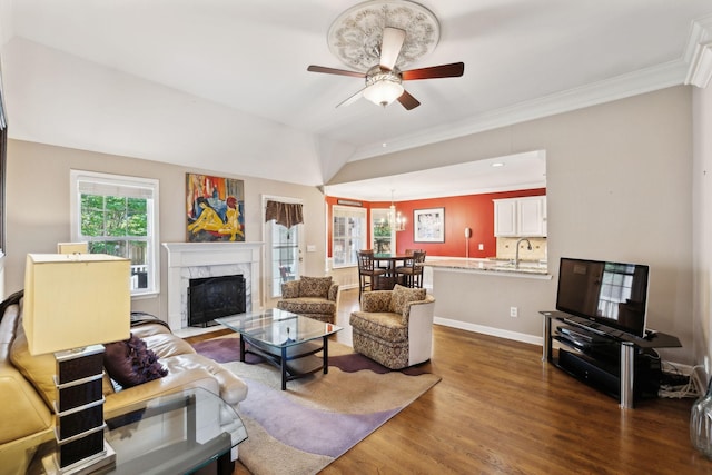 living area featuring wood finished floors, a ceiling fan, a premium fireplace, crown molding, and a chandelier