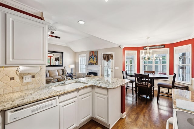 kitchen with white dishwasher, a peninsula, a sink, a high end fireplace, and tasteful backsplash