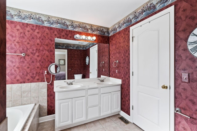 bathroom featuring tile patterned flooring, tiled tub, wallpapered walls, double vanity, and baseboards