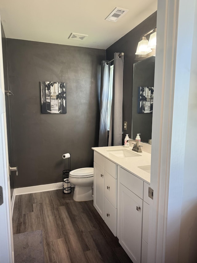 bathroom featuring wood finished floors, toilet, and double vanity