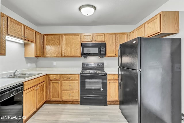 kitchen featuring black appliances, a sink, light wood finished floors, and light countertops