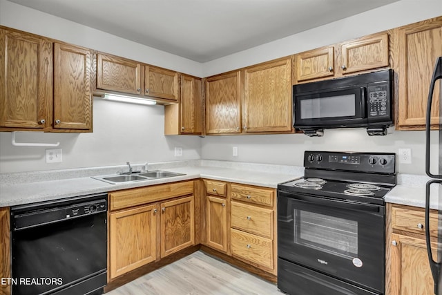 kitchen with black appliances, light countertops, light wood-style floors, a sink, and brown cabinetry
