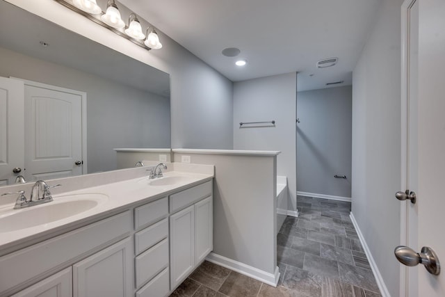 full bathroom with baseboards, double vanity, a bathtub, and stone finish floors